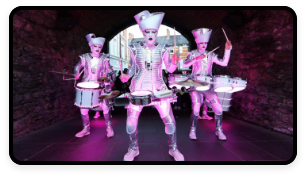 A trio of people are dressed in metallic costumes and playing drums.