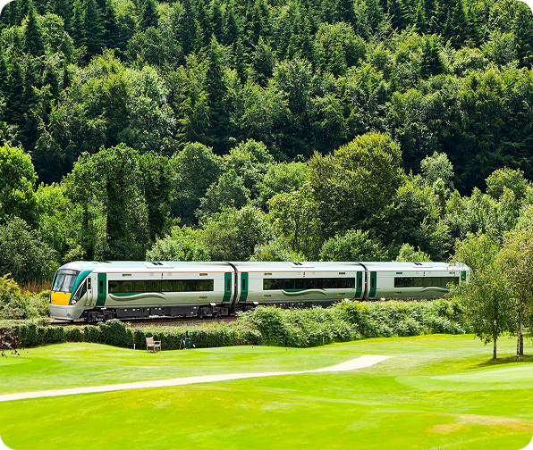 Green and white train traveling through rolling countryside surrounded by trees.