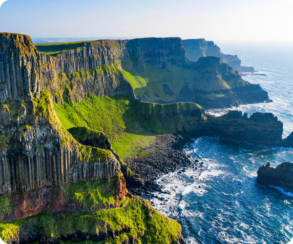 Steep green Causeway Cliffs with layered rock formations along a rugged ocean coastline in County Antrim. Steep green Causeway Cliffs with layered rock formations along a rugged ocean coastline in County Antrim.
