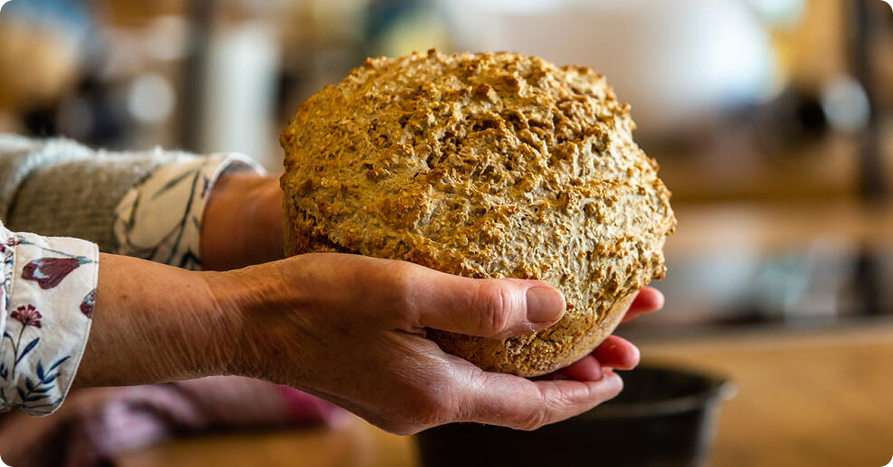 Hands holding a round rustic loaf of soda bread in a kitchen at Airfield Estate, Dublin. Hands holding a round rustic loaf of soda bread in a kitchen at Airfield Estate, Dublin.