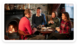 A group of people sitting a table next to a fireplace in a pub