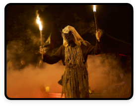 A masked figure holds up torches as part of the Samhain Festival.