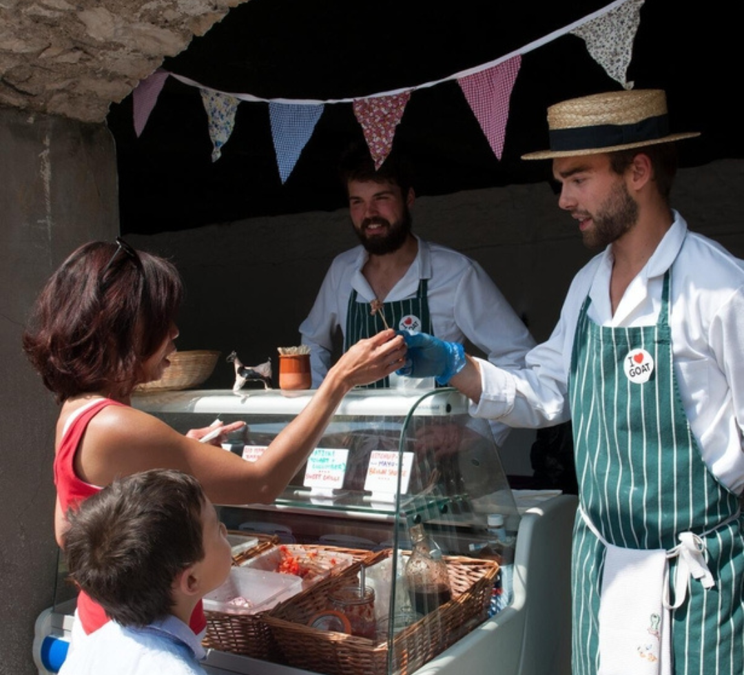 Two men in green aprons standing beside a food stall serving their produce.